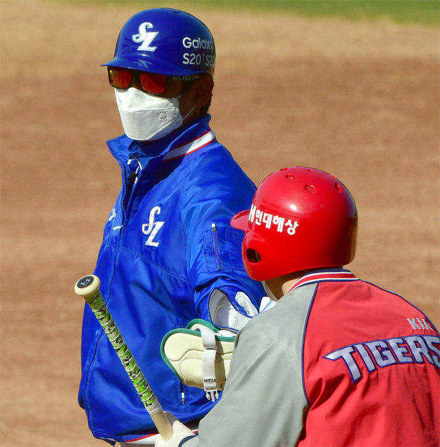 마스크를 쓰고 1루 코치 박스를 지킨 강명구 삼성 주루코치가 장갑을 낀 배트보이에게 장비를 건네고 있다. 광주=뉴스1·AP 뉴시스