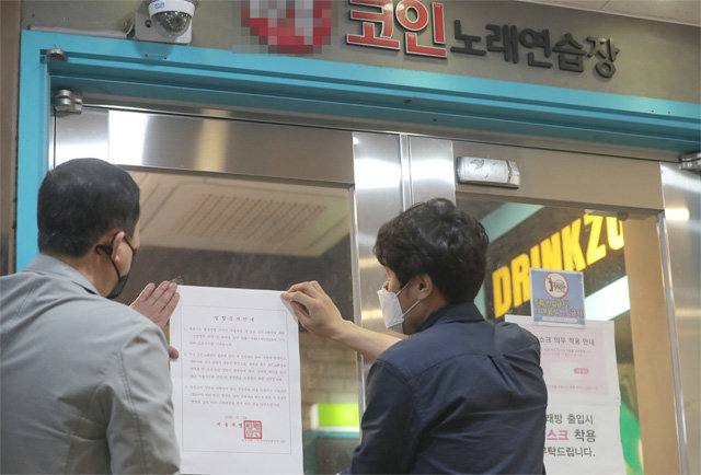 노래방을 통한 코로나19 감염 사례가 늘면서 서울시가 코인노래방에 집합금지 명령을 내린 22일 서울 종로구 관계자들이 관내 한 코인노래방 입구에 안내문을 붙이고 있다. 뉴스1