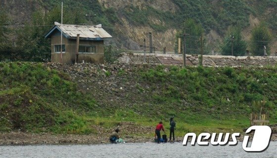 북-중 접경지에서 바라본 북한의 모습. 무채색 속 사이사이 보이는 사상문구와 북한 주민 및 국경 경비대, 뙈기밭의 모습에서 북한 주민의 현재 삶을 엿볼 수 있다. © News1