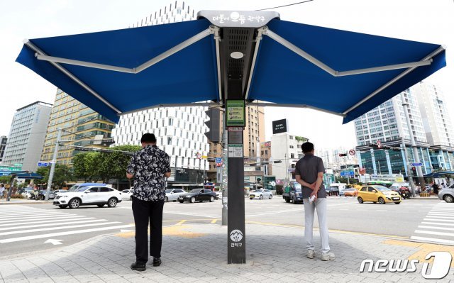 19일 서울 관악구 서울대입구역 앞에 설치된 ‘강감찬 스마트 그늘막’에서 시민들이 햇빛을 피하고 있다. ‘강감찬 스마트 그늘막’은 사물인터넷(IoT)과 태양광 기술로 온도, 바람, 일조량 등 주변 환경에 반응해 자동으로 개폐되는 그늘막이다. 2020.6.19/뉴스1 © News1