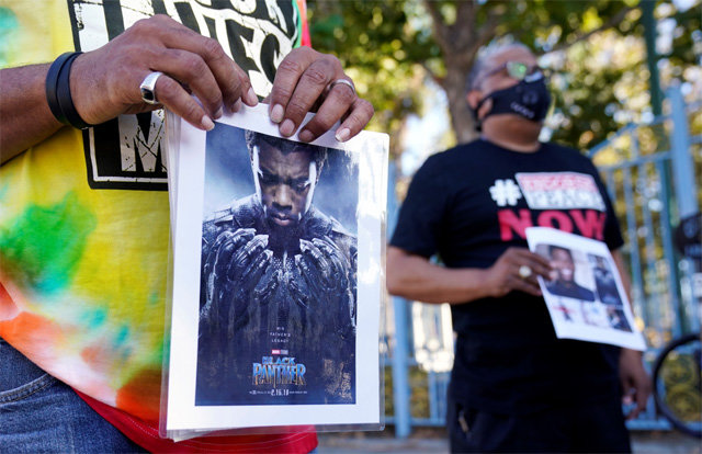 미국 로스앤젤레스에서 29일(현지 시간) 열린 배우 채드윅 보즈먼 추모 기자회견을 보러 온 시민들이 보즈먼이 주연한 영화 ‘블랙 팬서’ 포스터를 들어 보이고 있다. 로스앤젤레스=AP 뉴시스