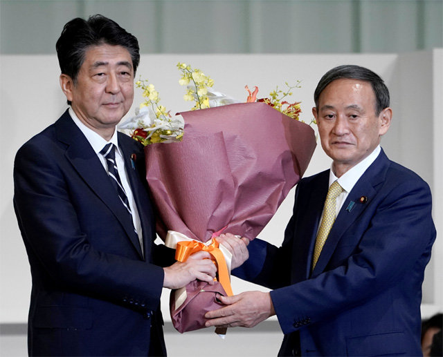 스가 요시히데 일본 관방장관(오른쪽)이 14일 열린 자민당 총재 선거에서 새 총재로 선출된 뒤 아베 신조 전 총재에게 감사의 꽃다발을 전하고 있다. 스가 신임 총재는 16일 임시국회에서 새 총리에 오른다. 도쿄=AP 뉴시스