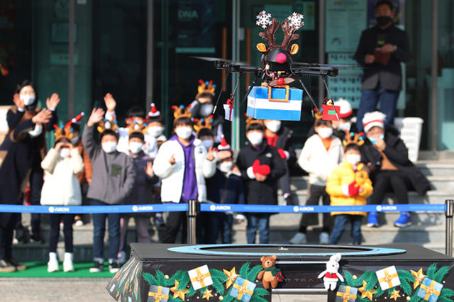 “산타 대신 루돌프 드론이 선물 싣고 왔어요” 크리스마스이브인 24일 오후 대구 수성구의 한 아동보육시설 마당에 루돌프 머리띠를 쓴 드론 한 대가 선물을 싣고 착륙하자 어린이들이 손을 흔들며 반기고 있다. 수성구는 신종 코로나바이러스 감염증 확산 방지를 위해 드론을 통한 비대면 방식으로 햄버거와 과자 등이 담긴 선물 상자를 전달했다. 대구=뉴스1