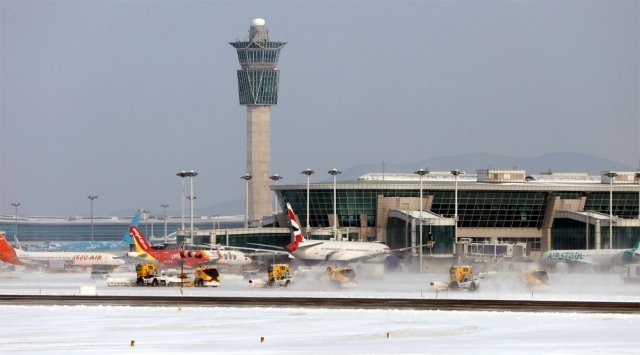 눈이 내린 인천국제공항 제1여객터미널 관제탑 인근 계류장에 비행을 마친 항공기가 서 있는 가운데 제설차량이 눈을 치우고 있다. 인천국제공항공사 제공