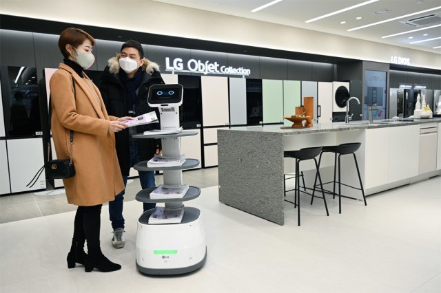 서울 서초구 LG베스트샵 서초본점을 찾은 고객들이 ‘LG 클로이 서브봇’이 갖다준 안내책자를 살펴보고 있다. LG전자 제공