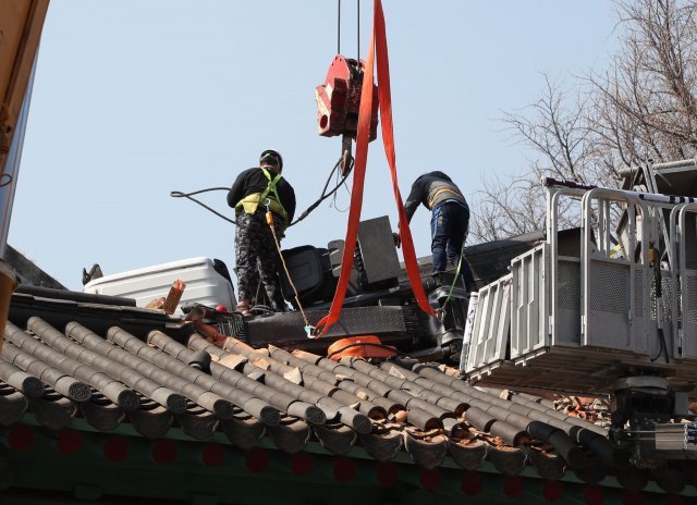 지붕위에 추락한 사다리차를 옮기기 위해 결박중인 작업자들.