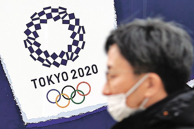 올림픽 상징물 앞을 지나는 마스크를 쓴 도쿄 시민. 신종 코로나바이러스 감염증(코로나19) 기세가 꺾이지 않아 일본 내 올림픽 재연기 또는 취소 여론도 커지고 있다. 도쿄=AP 뉴시스
