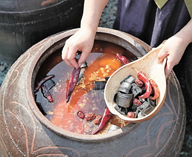 간장의 맛을 살리고 불순물을 제거하기 위해 붉은 고추와 숯을 독에 넣고 있다.