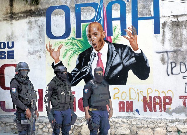 7일 무장한 아이티 경찰이 이날 새벽 괴한들의 총격에 암살당한 조브넬 모이즈 대통령의 사저 주변에서 경계 근무를 서고 있다. 경찰들 뒤로 모이즈 대통령이 연설하는 모습이 그려진 벽화가 보인다. 포르토프랭스=AP 뉴시스