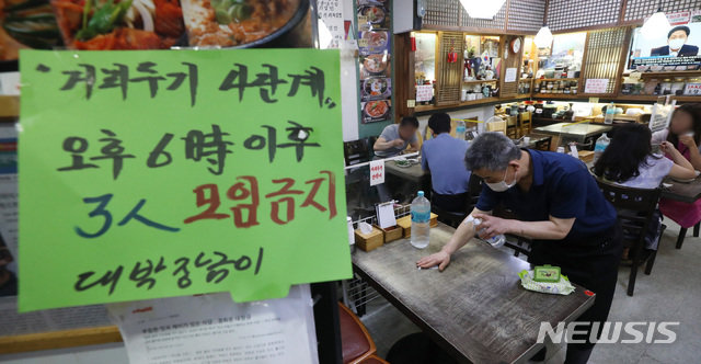 사회적 거리두기 4단계 첫날인 12일 서울 종로구 한 음식점에 붙은 오후 6시 이후 3인이상 모임 금지 안내문 너머로 사장이 테이블 소독을 하고 있다. 사진=뉴시스
