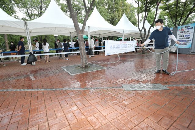 서울을 포함해 전국적으로 폭염이 기승을 부리는 가운데 서울 마포구 홍익문화공원에 마련된 임시선별진료소에서 구청 직원이 열기를 식히기 위해 바닥에 물을 뿌리고 있다.