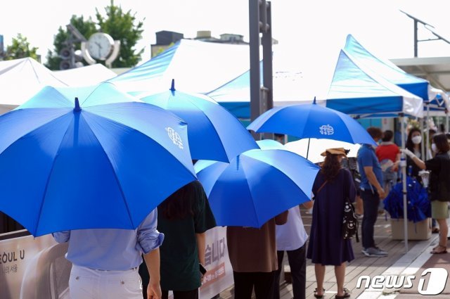 서울 성북구청 바람마당 선별진료소를 찾은 시민들이 폭염서울시, 코로나19-무더위 겹친 재난취약계층 특별 보호대책 실시대피용 파란우산을 쓰고 대기하고 있다.  (성북구제공) 2021.7.20/뉴스1