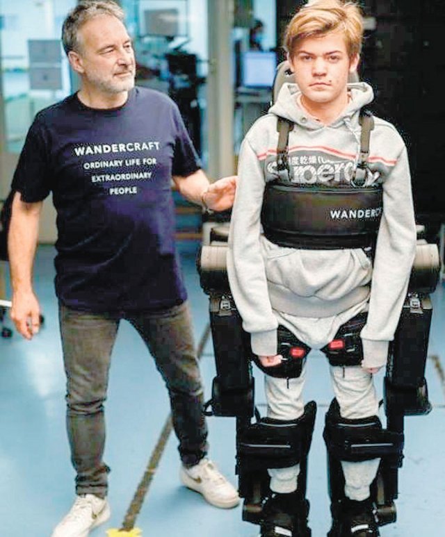 프랑스 로봇 개발 스타트업 ‘원더크래프트’의 장루이 콩스탕자 공동 창업자(왼쪽)가 하반신 불구인 아들 오스카르 군(16)에게 로봇슈트를 입힌 후 걷기 연습을 돕고 있다. BBC 화면 캡처