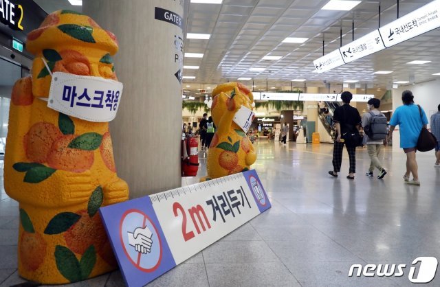 제주국제공항에서 마스크를 쓴 돌하르방 앞으로 관광객들이 지나가고 있다. 2020.8.30/뉴스1 © News1