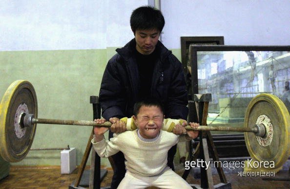 2005년 중국 청두 어린이 체조학교에서 한 소년이 코치의 도움으로 역기를 들어 올리고 있다. (GettyImages)/코리아