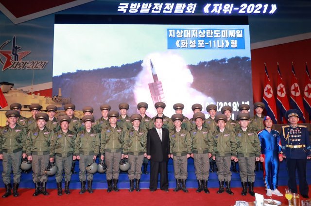 국방발전전람회 ‘자위-2021’에서 김정은 노동당 총비서가 비행사들과 기념사진을 찍고 있다.  이들 가운데 파란색 전신 타이츠를 입고 등장한 군인이 주목을 받고 있다.