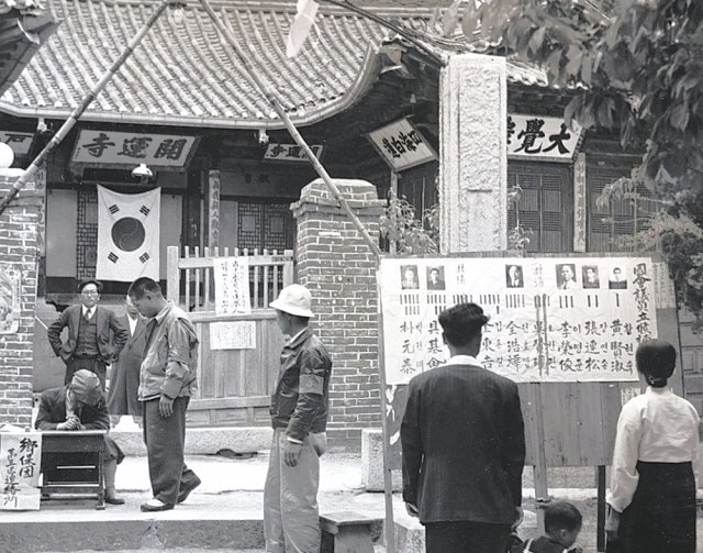 1948년 5월 10일 서울 개운사에 마련된 동대문을 지역구 투표소 앞에서 한 가족이 입후보자들의 선거공보를 보고 있다. 사진 출처 미국 국립문서기록청