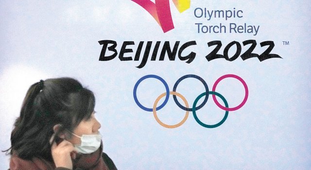 중국 베이징 시내에서 신종 코로나바이러스 감염증(코로나19)을 예방하기 위해 마스크를 쓴 여성이 2022 베이징 겨울올림픽 포스터 앞을 지나고 있다. 코로나19와 미국의 외교적 보이콧으로 베이징 겨울올림픽은 파란을 겪고 있다. 베이징=AP 뉴시스