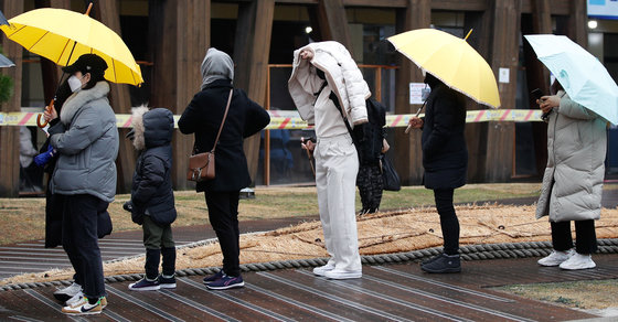 비가 내리는 15일 오전 서울 송파구보건소 선별진료소에서 코로나19 검사를 기다리는 시민이 외투를 뒤집어 쓰고 있다. 2021.12.15/뉴스1 © News1