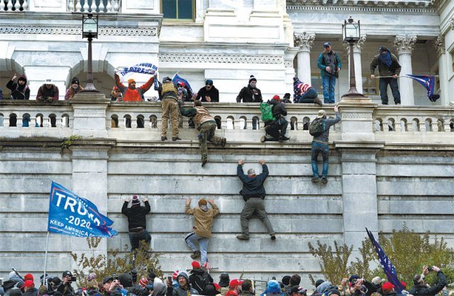 지난해 1월 6일 도널드 트럼프 당시 미국 대통령을 지지하는 폭력 시위대가 미국 워싱턴 국회의사당 웨스트홀 담벼락을 올라가고 있다. ‘트럼프’라고 적힌 파란 깃발이 곳곳에 보인다. 워싱턴=AP 뉴시스