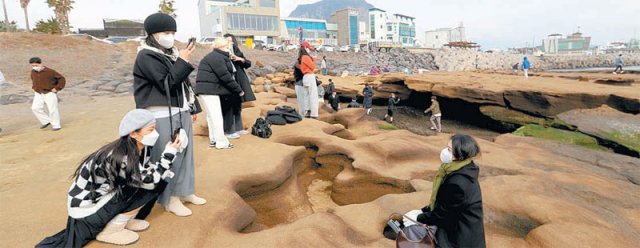 서귀포시 사계해변의 기암괴석 바위 구멍 틈 사이에서 사진을 찍고 있는 관광객들.