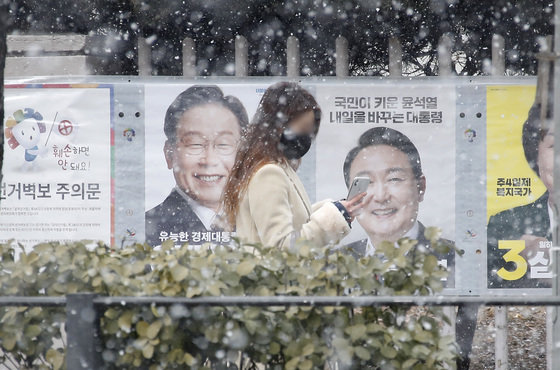 눈이 내리는 21일 서울 영등포구 여의도 KBS 인근에서 한 시민이 대통령 선거 벽보 옆을 지나고 있다. 2022.2.21/뉴스1 © News1 권현진 기자