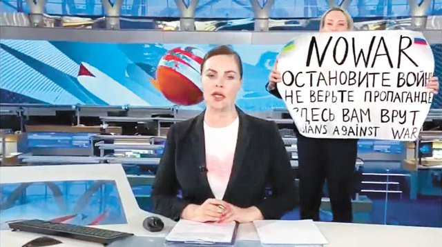 14일 러시아 국영TV ‘채널1’의 저녁 뉴스 생방송 중 러시아의 우크라이나 침공을 비판하는 문구를 들고 난입 시위를 벌인 편집자 마리나 오브샤니코바(오른쪽). 그는 우크라이나와 러시아 국기 사이에 ‘전쟁 반대(No War)’라는 문구가 쓰인 종이를 들었다. 이
 장면은 약 4초간 전파를 탔다. 야로슬라프 콘웨이 트위터 화면 캡처