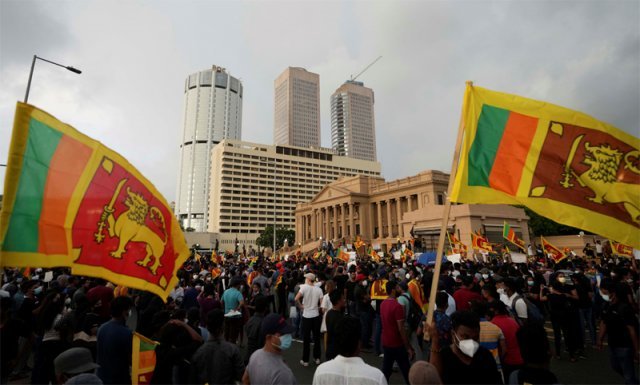 9일 스리랑카 수도 콜롬보에서 시민들이 국기를 흔들며 고타바야 라자팍사 대통령의 퇴진을 요구하고 있다. 시위대 뒤로 대통령 집무실 건물이 보인다. 콜롬보=AP 뉴시스