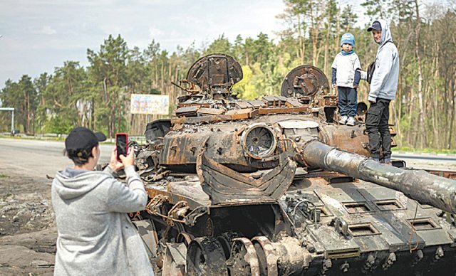 8일(현지 시간) 우크라이나 수도 키이우 교외에서 파괴된 러시아 탱크 위에 올라가 포즈를 취하는 아이들의 사진을 엄마로 보이는 여성이 찍어주고 있다. 키이우=AP 뉴시스