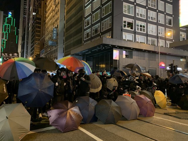 2019년 12월 홍콩의 한 거리에서 민주화 시위에 참가한 시민들이 검은 옷과 검은 마스크, 방독면 등을 쓰고 우산으로 바리케이드를 만들며 경찰의 공격에 대비하고 있다. 출처=참여연대 국제연대위원회
