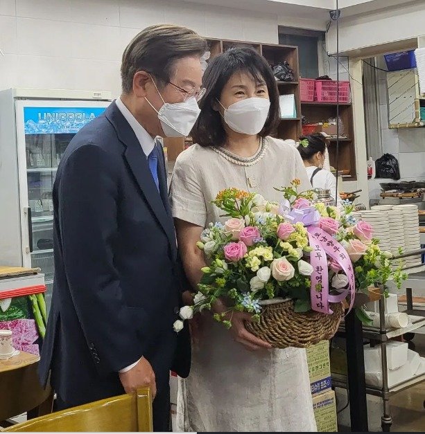 이재명 민주당 의원과 부인 김혜경씨가 지난 11일 지역구 모임에서 호남향우회로부터 축하 꽃바구니는 받고 활짝 웃고 있다. (SNS  갈무리) © 뉴스1