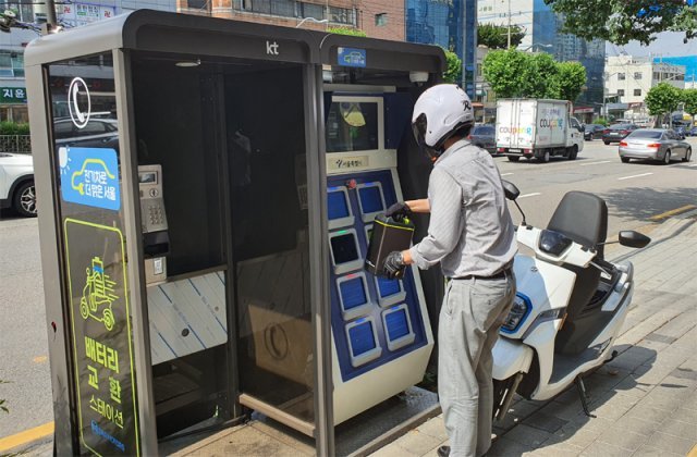 서울 관악구 구로전화국 앞 충전소에서 한 시민이 방전된 전기오토바이 배터리를 교체하고 있다. 서울시는 올해까지 낡은 공중전화부스 150곳에 전기오토바이 배터리를 교체할 수 있는 ‘교환형 충전소’를 설치할 예정이다. 서울시 제공
