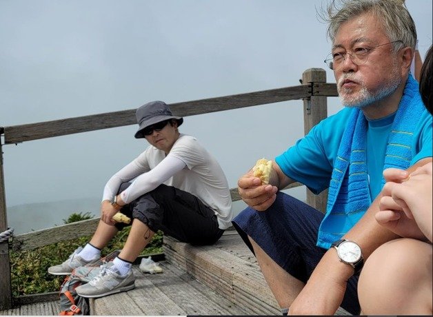 문재인 전 대통령이 4일 한라산 영실코스 등반 도중 휴식을 취하면서 옥수수를 맛있게 먹고 있는 모습을 탁현민 전 의전비서관이 물끄러미 바라보고 있다. (페이스북 갈무리) ⓒ 뉴스1