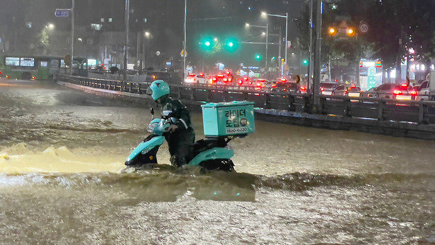 중부지방을 중심으로 폭우가 쏟아진 8일 밤 서울 관악구 도림천이 범람, 주변을 지나는 배달 라이더가 아슬아슬하게 물살을 헤치며 바이크를 옮기고 있다. 뉴스1