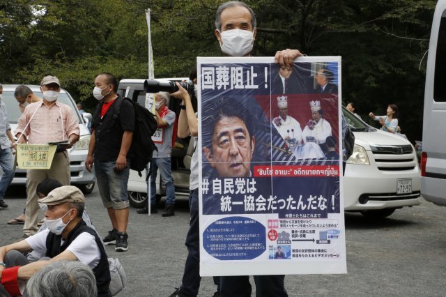 23일 일본 도쿄의 한 공원에서 한 남성이 아베 신조 전 일본 총리의 국장에 반대하는 포스터를 들고 시위에 참여하고 있다. 2022.09.23. AP/뉴시스