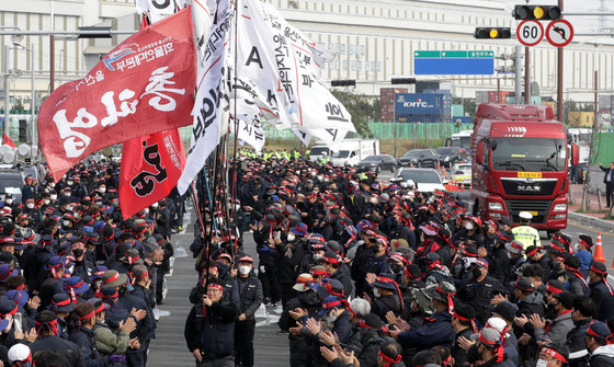 24일 울산 남구 울산신항 앞에서 민주노총 전국공공운수노동조합 화물연대 울산본부 총파업 출정식이 열린 가운데 입장하는 깃발 뒤로 화물차가 지나가고 있다. 2022.11.24/뉴스1 ⓒ News1