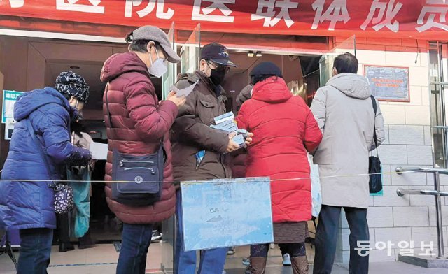 19일 중국 베이징 차오양구의 한 발열진료소에서 진료를 받기 위해 대기하는 줄이 건물 밖으로 이어져 
있다. 진료 대기 줄 사이로 검은 모자를 쓴 한 남성이 양손에 약을 받아 들고 나오고 있다. 베이징=김기용 특파원 
kky@donga.com