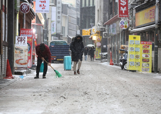 서울을 비롯해 중부지방에 대설특보가 발효된 21일 오전 서울 명동거리에서 상인이 쌓인 눈을 치우고 있다. 2022.12.21/뉴스1