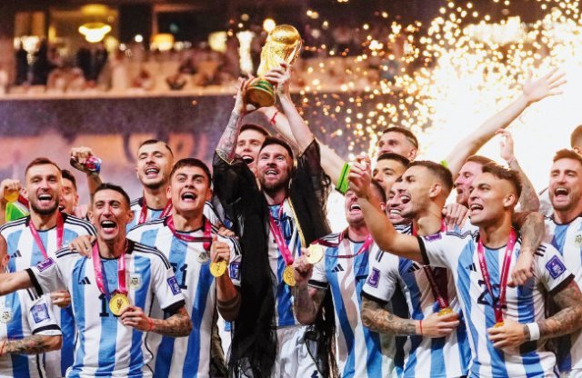 Messi (centro) e jogadores argentinos comemoram enquanto levantam o troféu do campeonato vestindo roupas tradicionais árabes 