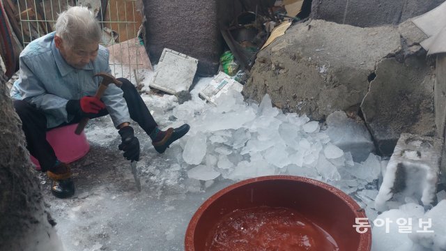 지난해 12월 27일 서울 강남구 구룡마을에서 주민 최소임 씨(95·여)가 부엌칼로 얼음을 부수고 있다. 최 씨는 한파로 수도관이 얼어붙어 물이 일주일 넘게 끊기자 얼음을 녹여 물을 구하고 있었다. 이승우 기자 suwoong2@donga.com