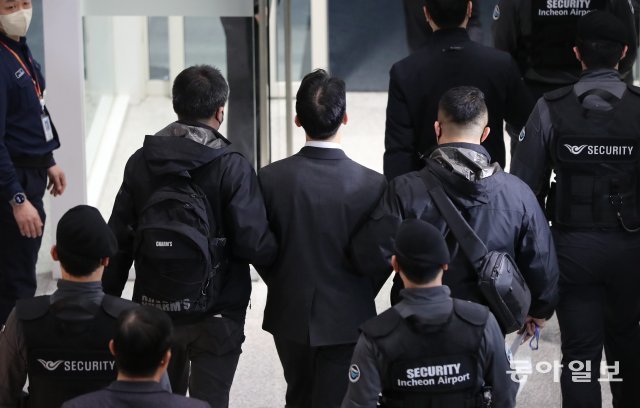 많은 형사들과 공항 보안요원들에게 둘러싸여  이송되고 있다.    이훈구 기자 ufo@donga.com
