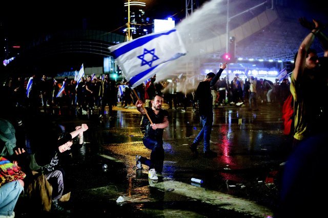 지난달 27일 이스라엘 텔아비브에서 열린 ‘사법부 무력화’ 법안 반대 시위에 나온 시민이 경찰의 물대포를 맞으며 이스라엘 국기를 흔들고 있다. 텔아비브=AP 뉴시스