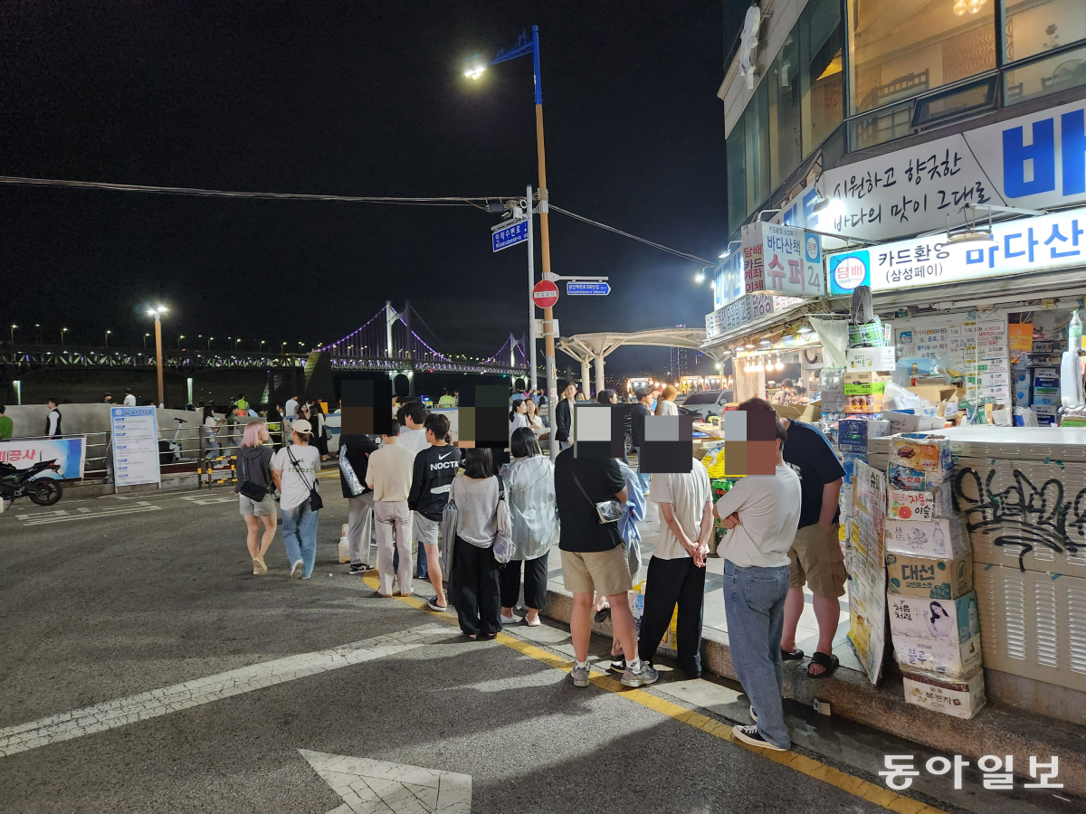 24일 밤 부산 수영구 민락수변공원 앞 포장회 가게 앞에 긴 줄이 늘어서 있다. 민락수변공원은 2000년대 중반부터 근처 가게에서 생선회와 치킨 등을 포장해와 술을 즐기는 명소로 유명해졌다. 김화영 기자 run@donga.com