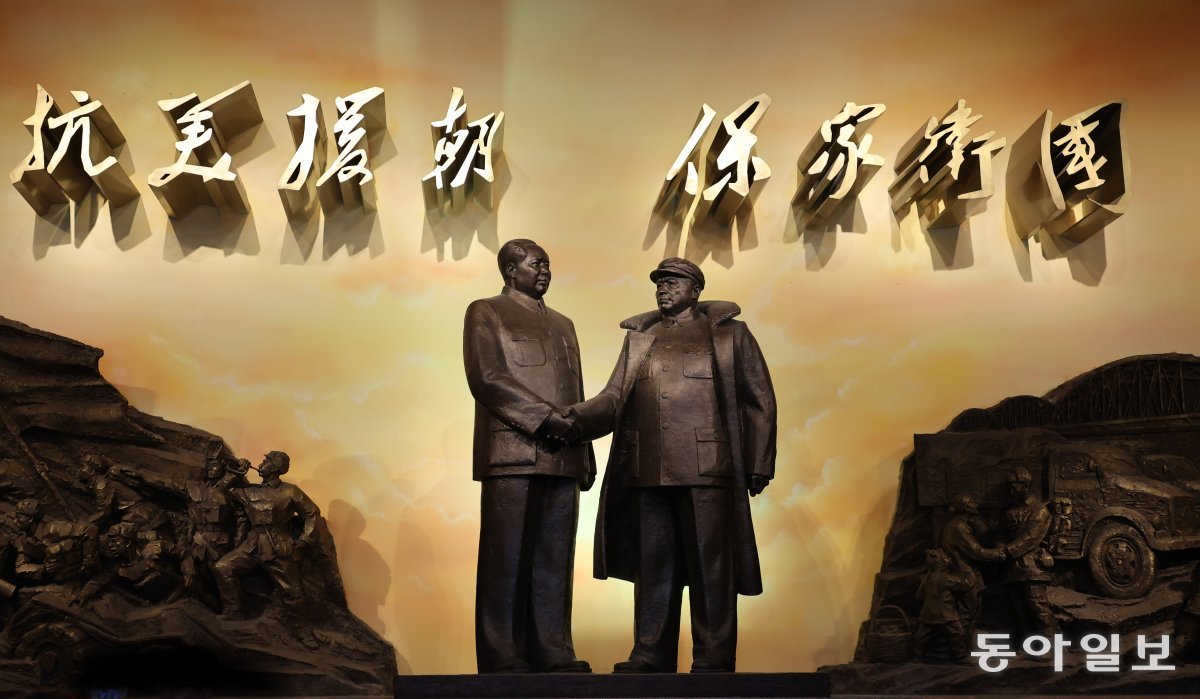 중국 단둥 항미원조기념관 내부 전시관 초입에 있는 마오쩌둥과 펑더화이가 악수를 하는 대형 동상. 뒤로 ‘미국에 대항해  조선(북한)을 돕고, 가족과 나라를 지킨다’는 중공이 내세운 참전 명분이 적혀 있다. 단둥 = 홍진환 기자