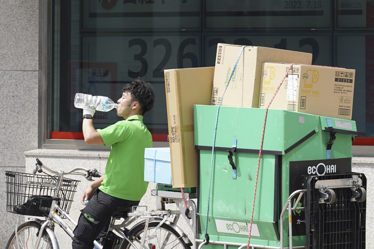 18일 일본 도쿄의 한 증권회사 앞에서 배달원이 일본의 닛케이 225 지수를 보여주는 전광판 앞에서 물을 마시고 있다. 도쿄=AP 뉴시스