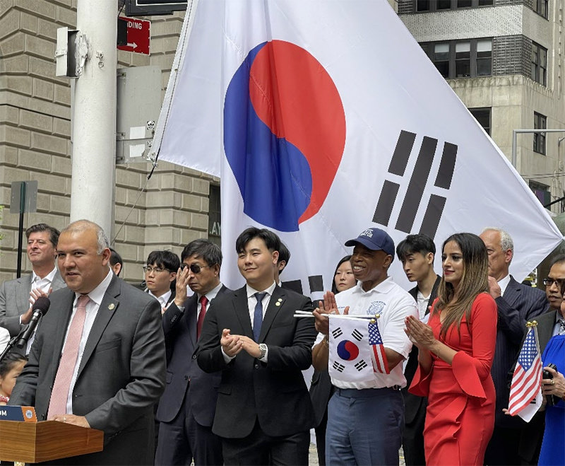 광복절을 맞아 14일(현지 시간) 미국 뉴욕 맨해튼 월스트리트에 있는 황소상 앞에 태극기가 게양돼 있다. 이를 배경으로 브라이언 파크 재미차세대협의회(AAYC) 이사와 에릭 애덤스 뉴욕시장(모자 쓴 남성)이 박수를 치고 있다. AAYC 제공