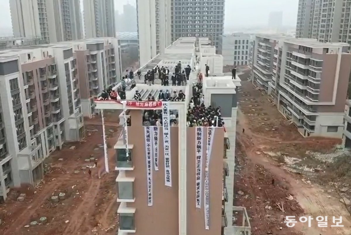 중국 장시성 난창시의 한 미완공 아파트 옥상에서 주택을 분양받은 사람들이 공사를 재개하라고 요구하고 있다. 아파트 벽에 걸린 시위 현수막에는 ‘신용 상실’, ‘약속 미이행’ 등이 적혀 있다. (NYT)