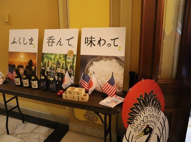 18일(현지시간) 미국 워싱턴 연방의회 의사당에서 열린 후쿠시마산 초밥 파티. “후쿠시마, 마시고 맛보세요”라고 적힌 팻말이 놓여 있다. 테이블 위에는 후쿠시마에서 빚은 일본주와 전통 술잔(마스)가 성조기와 함께 장식돼 있다. 출처 : 주미 일본대사관