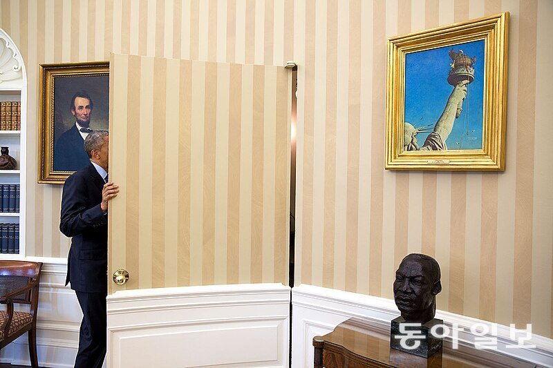 백악관 집무실 문을 나가는 버락 오바마 대통령 옆쪽으로 보이는 마틴 루터 킹 목사 조각상과위쪽에 걸린 그림 ‘자유의 여신상에서 일하며’(Working on the Statue of Liberty). 위키피디아