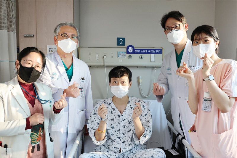 30대 남성 이모 씨(가운데)가 지난해 12월 서울 송파구 서울아산병원에서 인공심장 삽입술을 받고 퇴원 전 의료진과 ‘손가락 하트’를 만들며 사진을 찍고 있다. 서울아산병원 제공